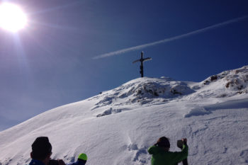 Skitourengeher auf einem Gipfel mit Gipfelkreuz