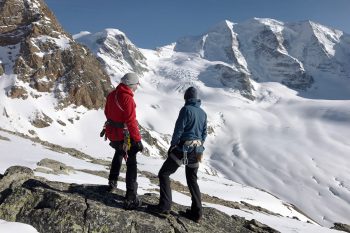 Zwei Bergsteiger mit Klettergurt vor dem Gipfelaufbau im Schnee.