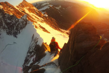Begrsteiger auf einem steilen Berggrad, der in orangenes Sonnenlicht getaucht ist.