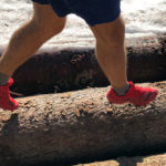 Die Füße eines Läufers mit Salomon Speedcross 5 Laufschuhen über einen Baumstamm laufend.