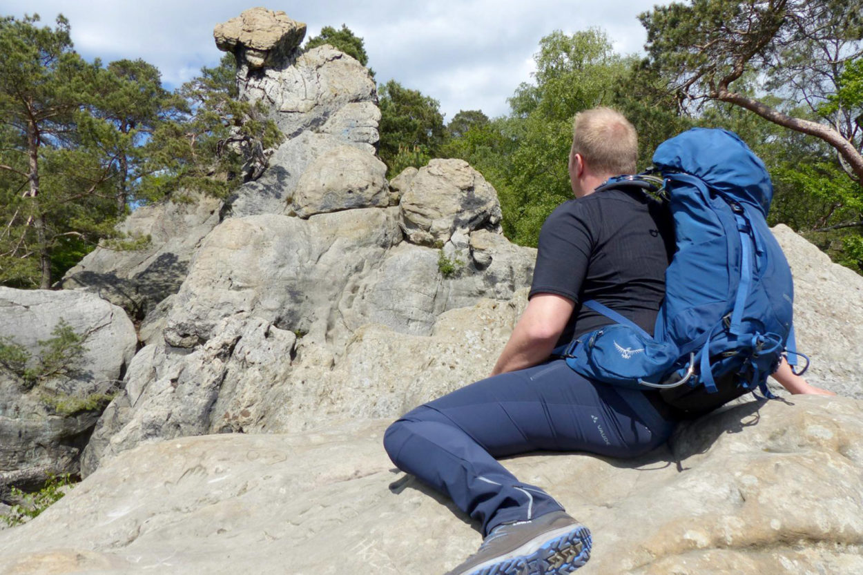 Ein Wanderer sitzt auf einem Felsen und blickt in die Landschaft