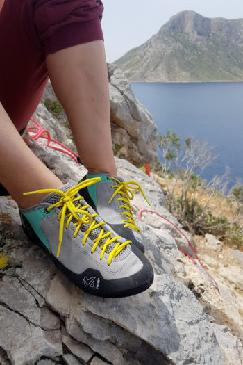 Kletterin mit 3/4 Hose in Weinrot trägt Millet Rock Up und sitzt auf Fels mit Blick auf Meer und vorgelagerte Insel