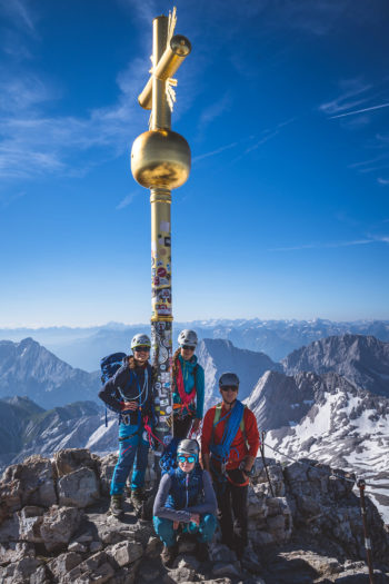 Gruppe von Wanderern steht vor goldenem Gipfelkreuz auf der Zugspitze